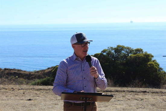 Asm. Hart at podium, speaking, with ocean in background