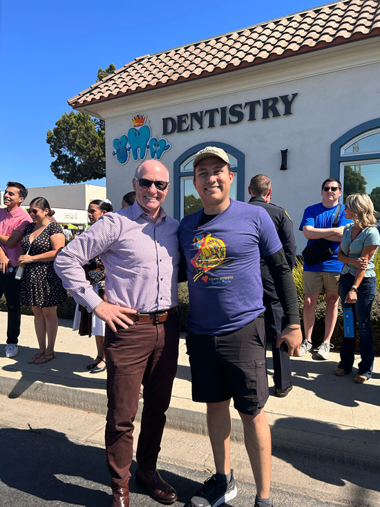 Asm. Hart and constituent posing in front of dentist's office, with multiple constituents in background