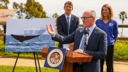 Asm. Hart at podium, speaking, with large whale poster at left