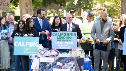 Asm. Hart at podium, speaking, with recyclables piled in foreground
