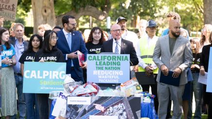 Asm. Hart at podium, speaking, with recyclables piled in foreground