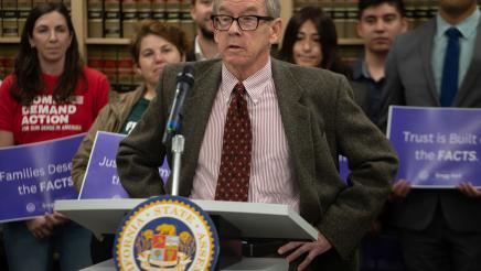 Guest speaker at podium, speaking, as suppporters listen on