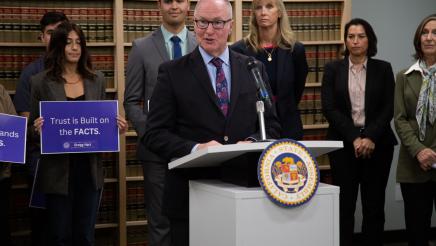 Asm. Hart at podium, speaking, as suppporters listen on
