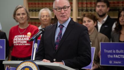 Asm. Hart at podium, speaking, as suppporters listen on